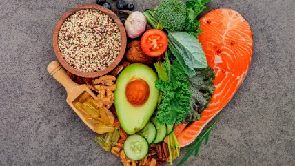 Food combining for nutrient absorption: avocado, salmon, broccoli, quinoa, nuts, and vegetables in heart shape on stone background