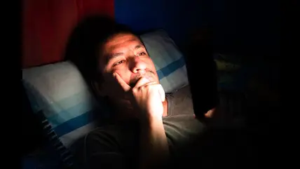 Man lying in bed at night using phone, disrupting sleep chronotype and circadian rhythm