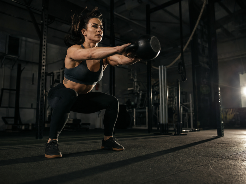 Person doing kettlebell swings in a dark gym, dynamic exercise for weight loss