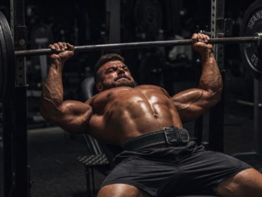 Muscular athlete performing a barbell bench press in a dark dramatic gym