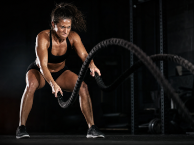 Athletic woman performing rope battle slams in a dark intense gym