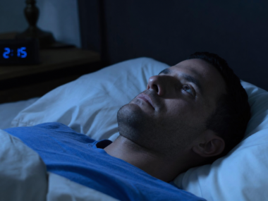 Person lying awake in bed at night staring at ceiling representing insomnia causes and solutions