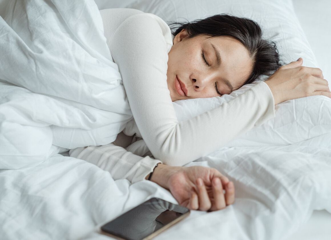 Woman sleeping in bed near smartphone with screen glow at night
