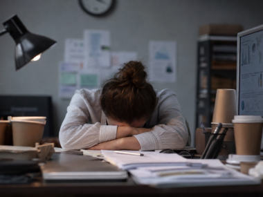 Exhausted person with head on desk representing sleep deprivation effects on brain and body
