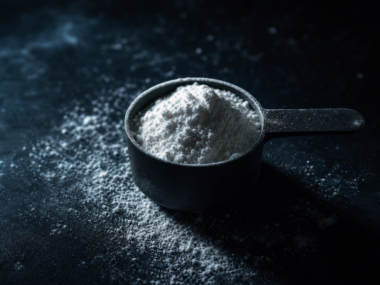Creatine monohydrate powder scoop and capsules on dark gym surface