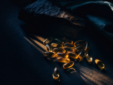 Vitamin D3 capsules with sunlight rays on dark surface